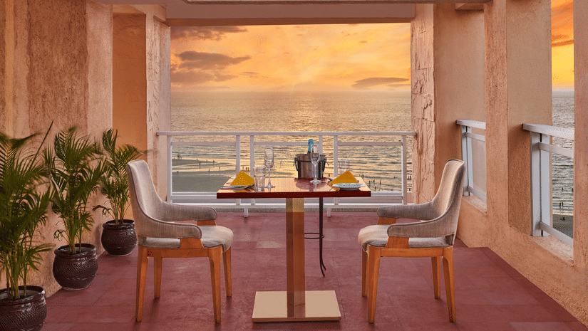 Open terrace dining setup at The Resort, Mumbai overlooking the sea during sunset, with a table for two, warm lighting, and coastal views creating a relaxed ambience.