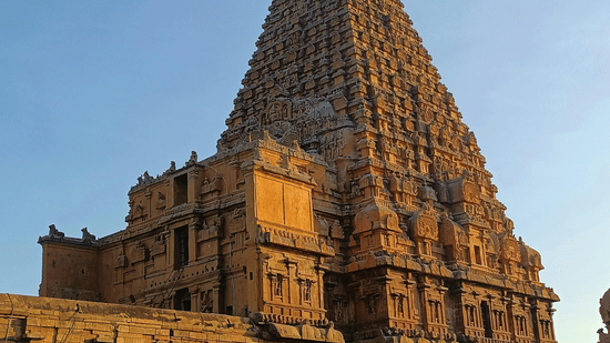 A towering, pyramid-shaped temple structure, known as a gopuram, stands on a green lawn against a clear blue sky.