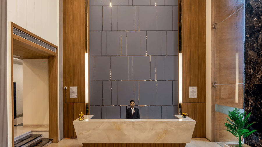 A modern hotel lobby with a marble front desk, elegant lighting, and stylish wall panels, featuring a colourful floral carpet at its centre.