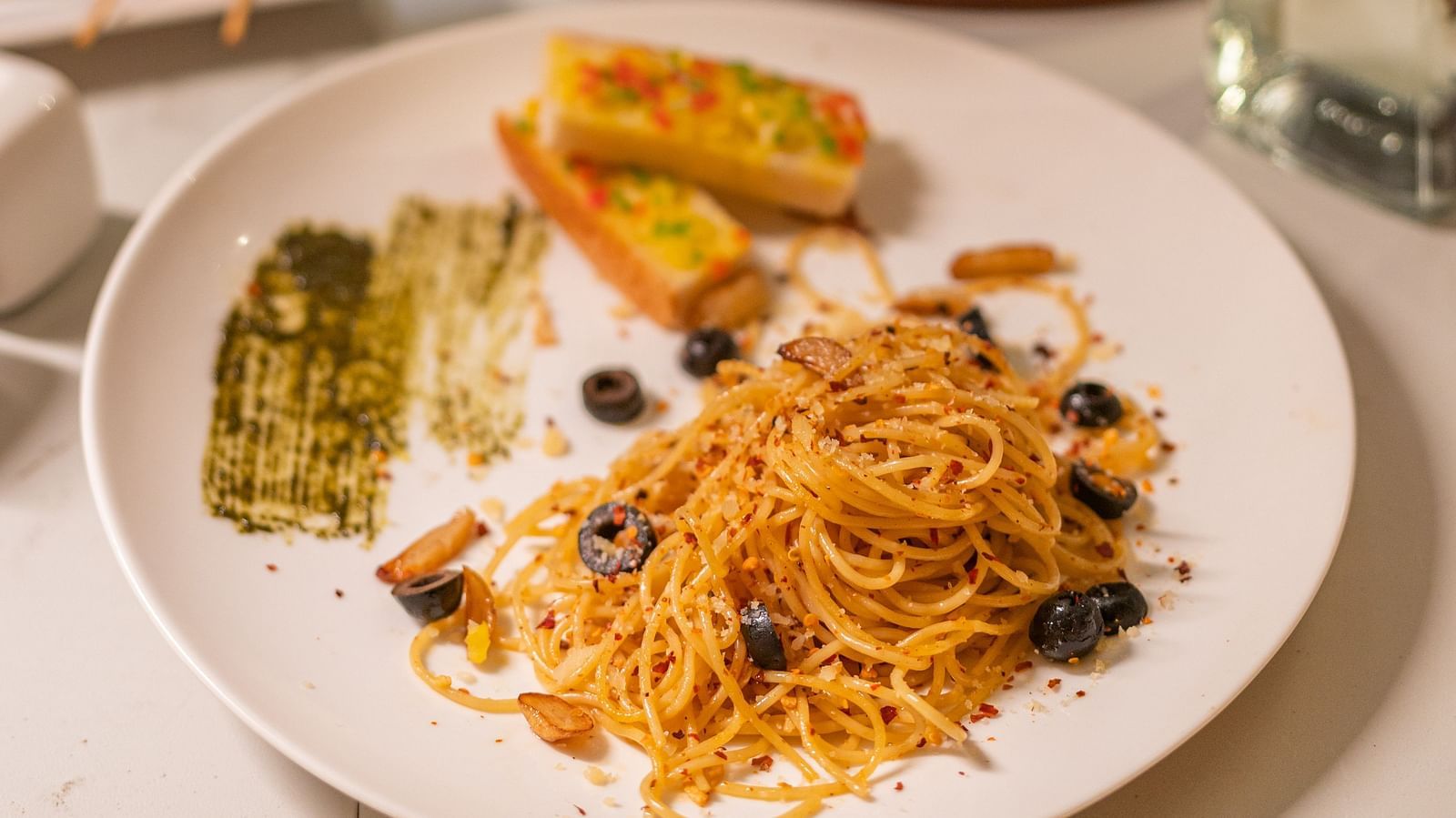 image of spaghetti served with two slices of garlic bread well plated on white porcelain dish - Darza Resorts