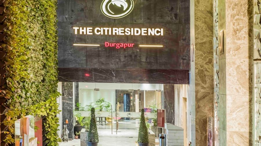 Hotel entrance with a vertical sign displaying The Citi Residenci and greenery around the doorway.
