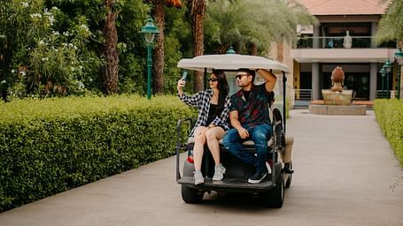 A couple taking selfies while seated in the back of a golf cart, enjoying their ride at Crescent Spa & Resort, Indore