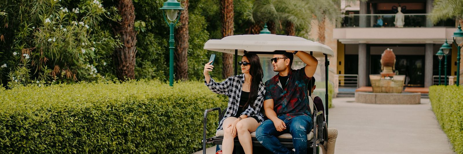 A couple taking selfies while seated in the back of a golf cart, enjoying their ride at Crescent Spa & Resort, Indore