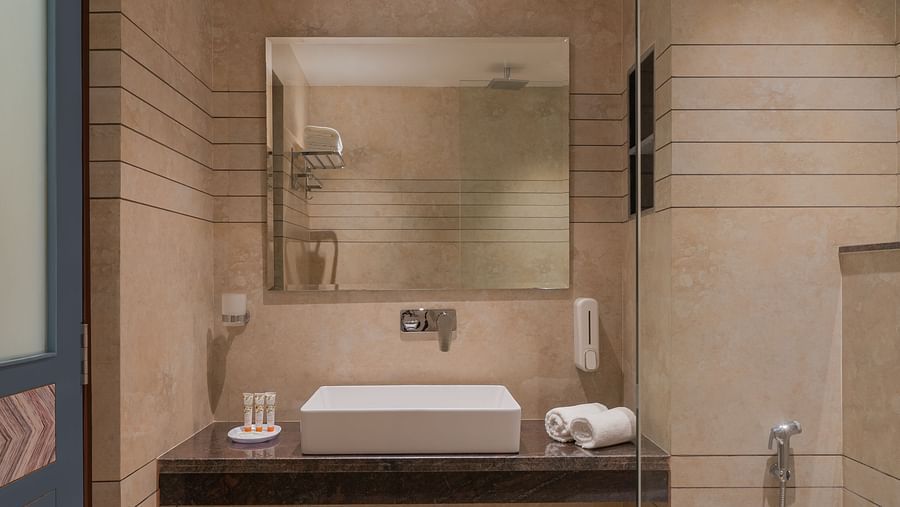 A spacious bathroom featuring a wall-mounted mirror above a wash basin and a western-style toilet | Hotel Ganga Maiya