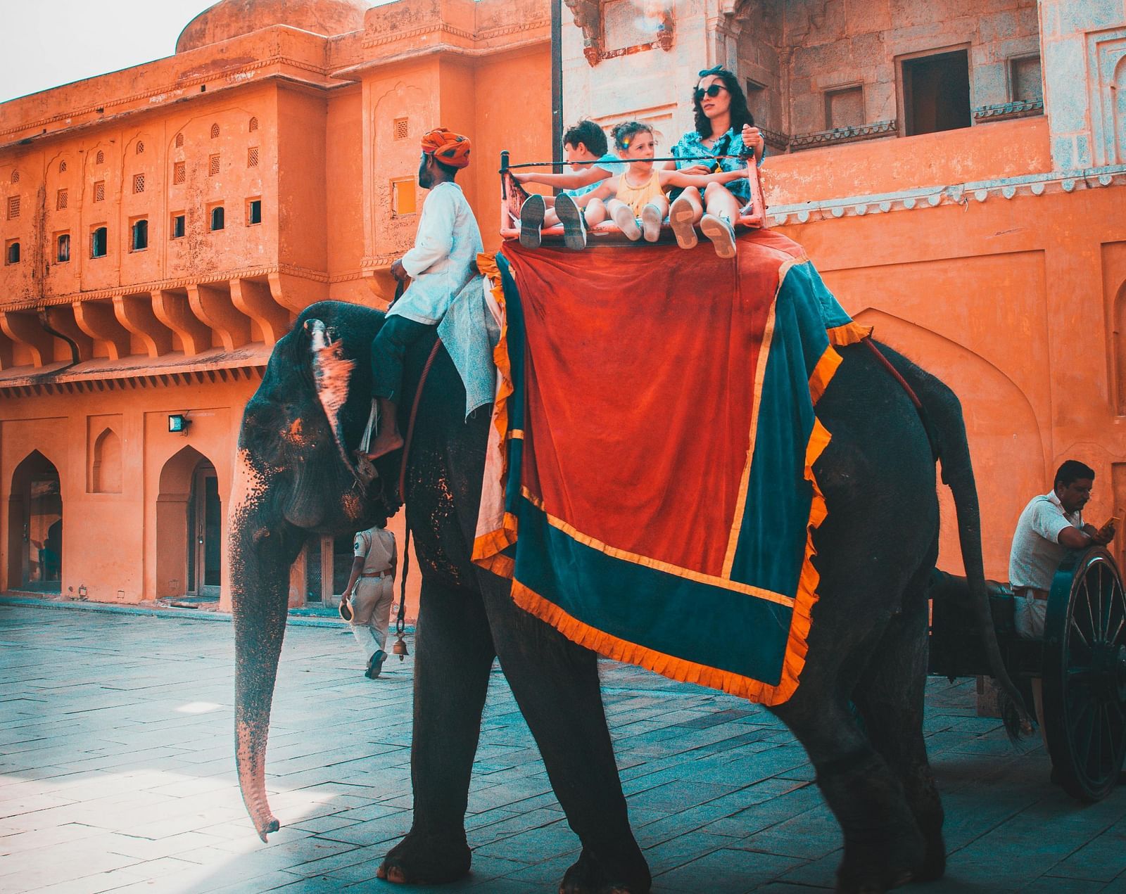 Tourists ride an elaborately decorated elephant near the majestic Amber Fort in Jaipur, bathed in warm sunlight.