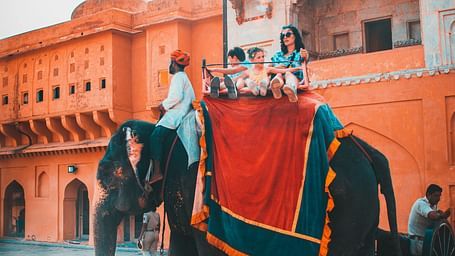 Tourists ride an elaborately decorated elephant near the majestic Amber Fort in Jaipur, bathed in warm sunlight.