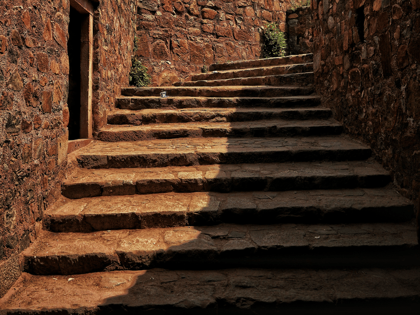 A narrow stone staircase leading upwards between high stone walls into a bright blue sky.