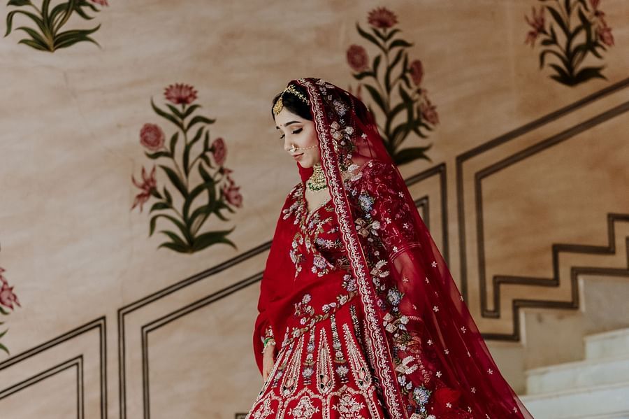 A bride walks down a staircase in a traditional lehenga, with floral wall designs- Umaid Palace - Best Luxury Heritage Resort Near Jaipur.
