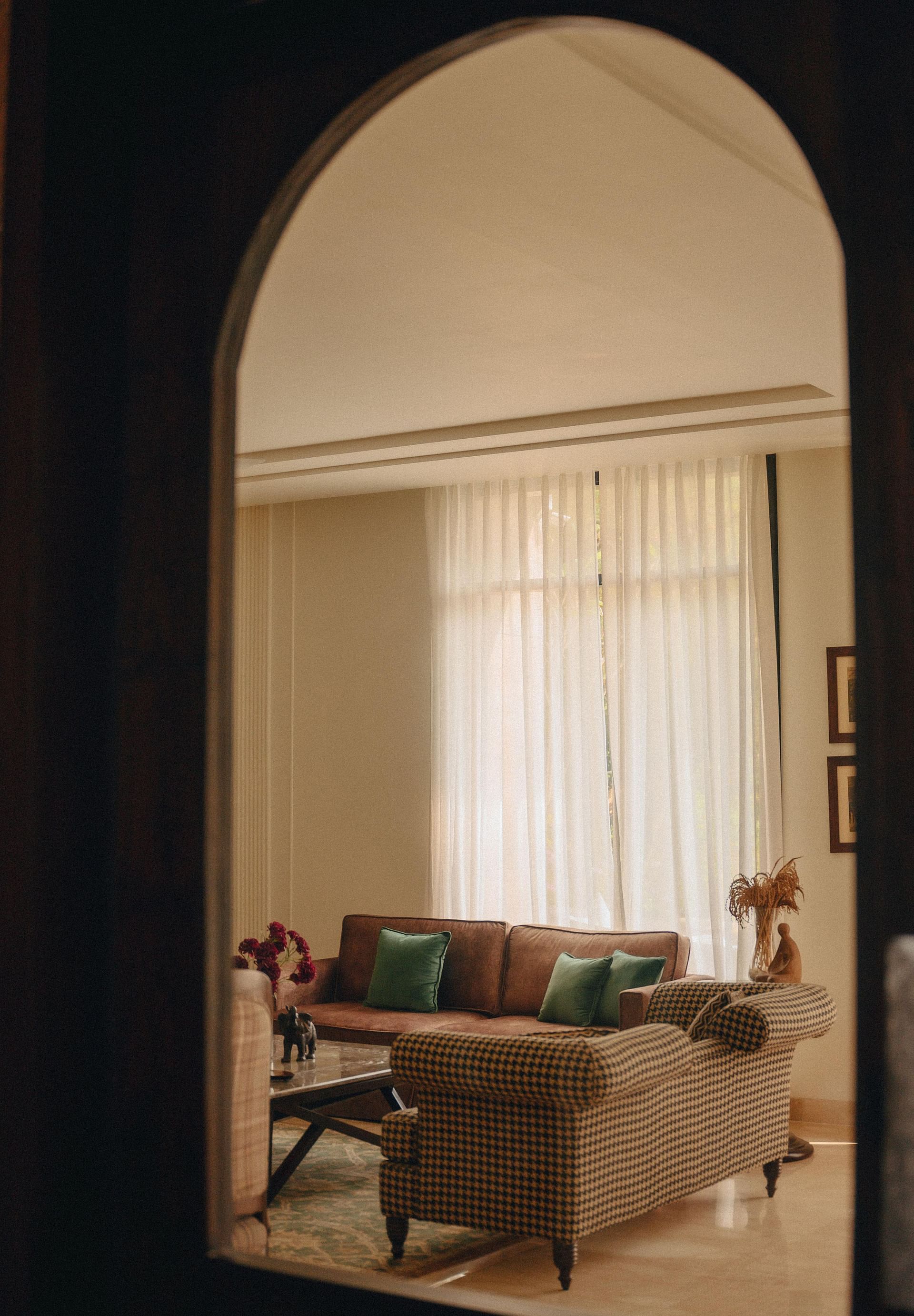 Interior view at Karma Chalets showing a hallway arch with a curtain and a sofa placed near a window with soft lighting.