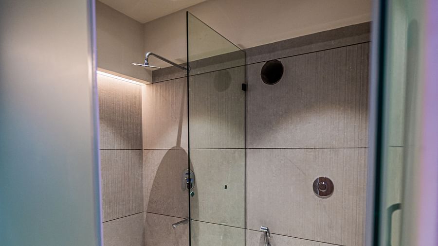 A western toilet separate from the shower area, enclosed with glass panels, at Indie Stays Mumbai International Airport.
