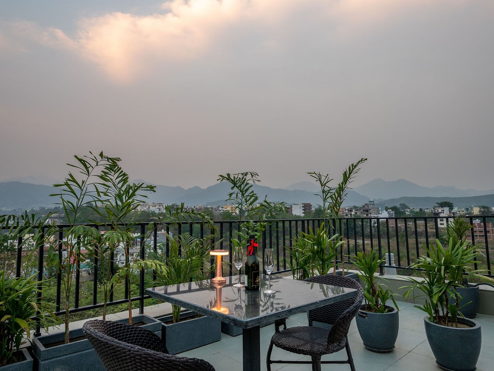 Close up of an outdoor seating area at Vishranti Hotel, Dehradun with a seating area features multiple tables with chairs, and plants are visible in the background.