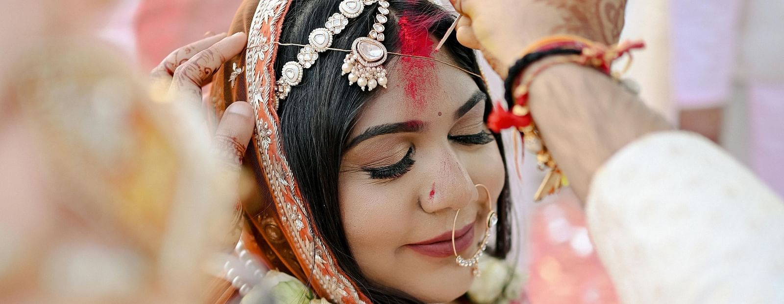 A close-up of a woman in traditional wedding attire, with a veil and jewelery, during a ceremonial moment at a wedding