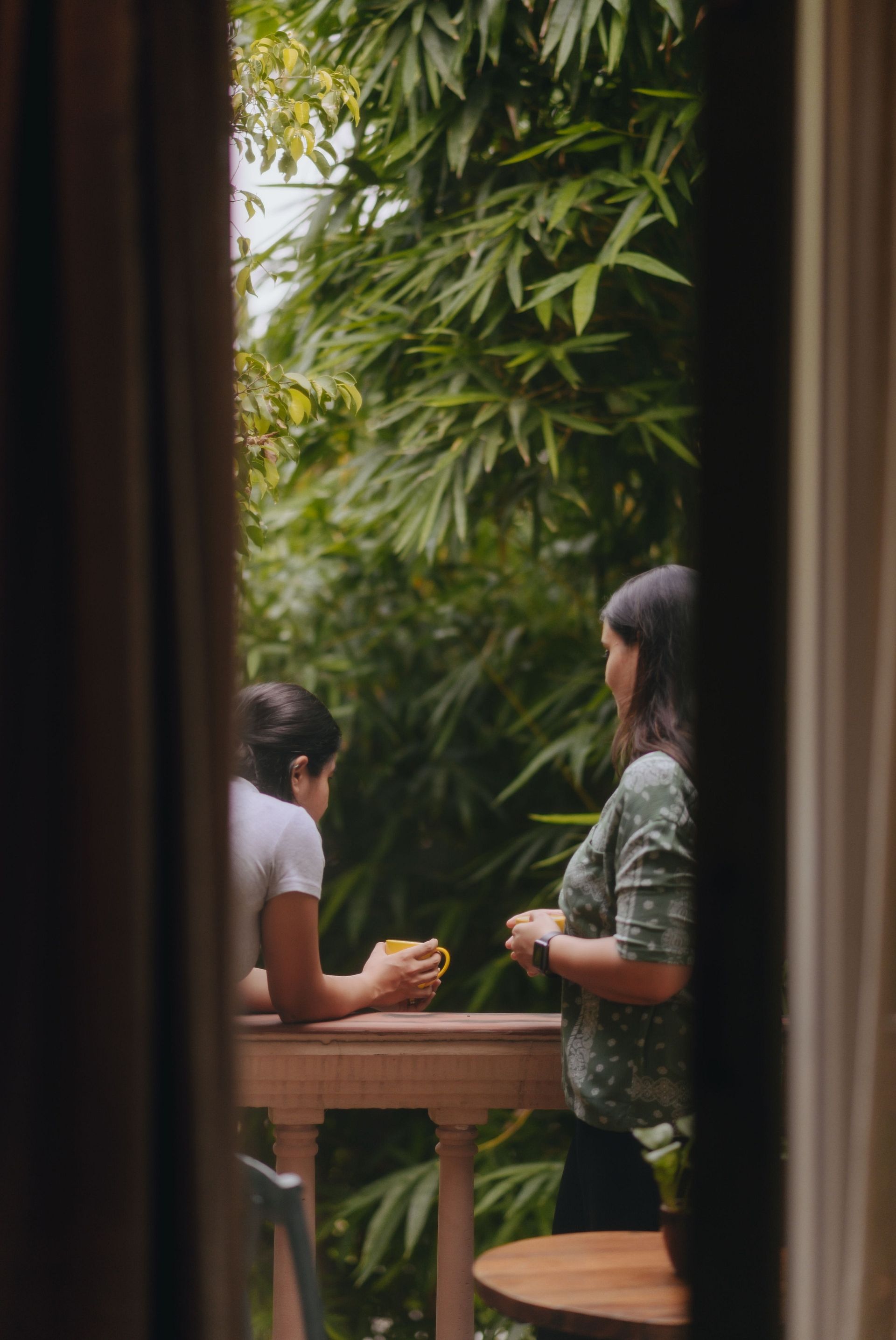Door opening to two women leaning on the balcony parapet which offers a view of the lush trees ahead - Karma Chalets