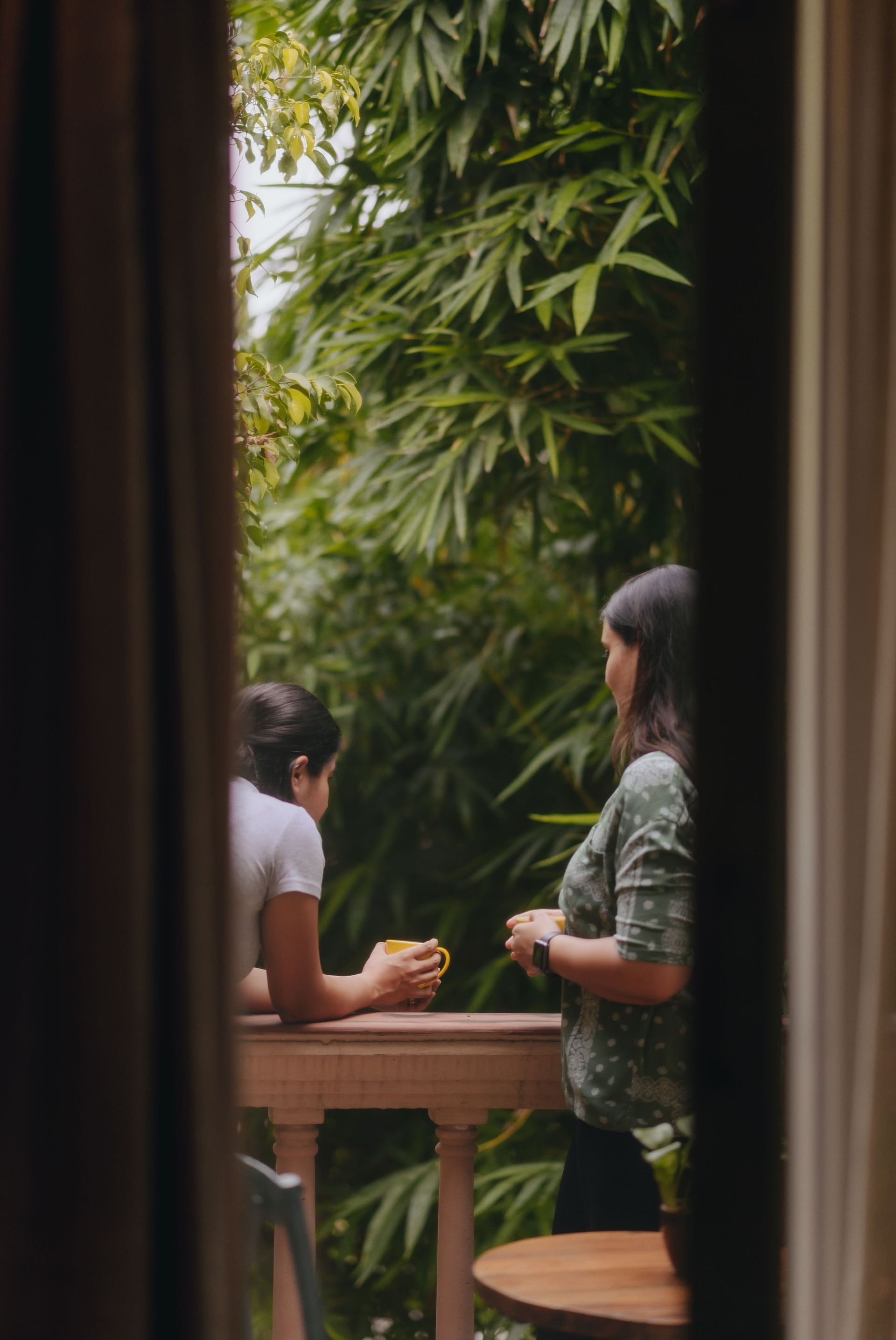 Door opening to two women leaning on the balcony parapet which offers a view of the lush trees ahead - Karma Chalets