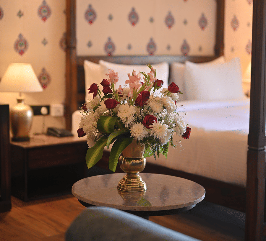 A  Premium Tent featuring a flower vase placed on a table and at the background there is a bed, a bedside table with lamp and a telephone at The Baagh Ananta Elite, Ranthambore