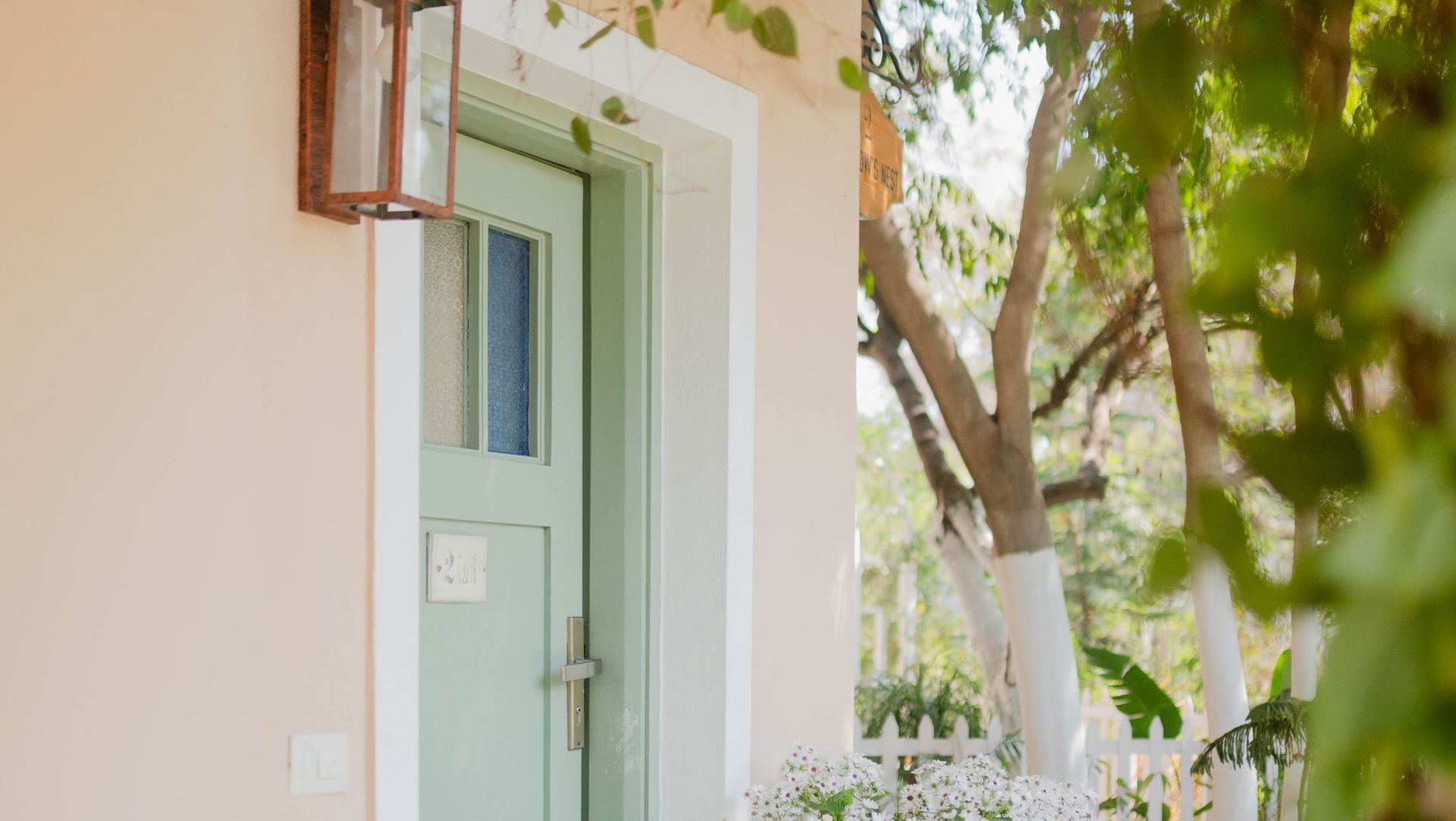 Charming villa entrance with a pastel green door, potted flowers, and a white picket fence at Karma Chalets.
