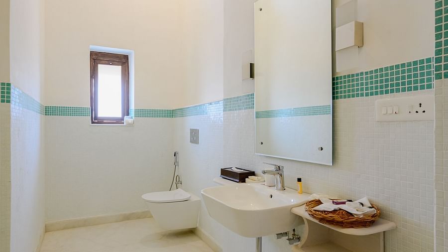 A long, narrow bathroom with a white sink, mirror, and a small window, accented with teal trim, in a vertical shot - Tijara Fort-Palace - 19th Century, Alwar.