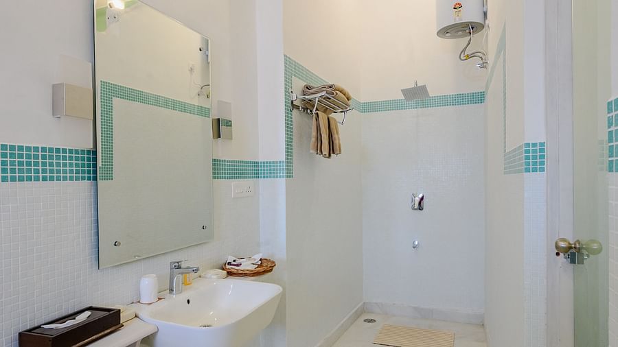 A narrow bathroom with a sink, mirror, and shower, featuring white walls and teal accents, in a vertical shot - Tijara Fort-Palace - 19th Century, Alwar.