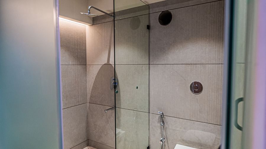 A western toilet separate from the shower area, enclosed with glass panels, at Indie Stays Mumbai International Airport.