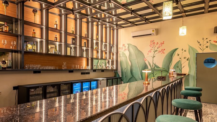 A bar featuring a long bar counter with stools, a well-stocked back bar, and decorative ceiling panels at Vishranti Hotel, Dehradun.