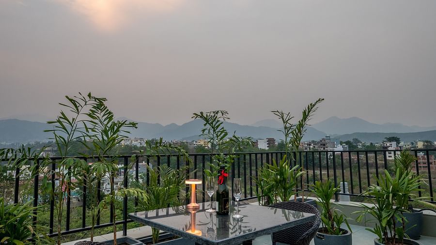 Close up of an outdoor seating area at Vishranti Hotel, Dehradun with a seating area features multiple tables with chairs, and plants are visible in the background.