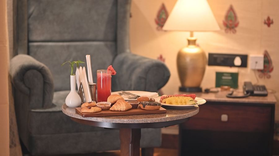 A Premium Tent featuring a sofa chair, a centre table which has a tray with croissant, cookies, doughnuts, a glass of juice and near to it there is a bedside table  with lamp and a telephone - The Baagh Ananta Elite, Ranthambore