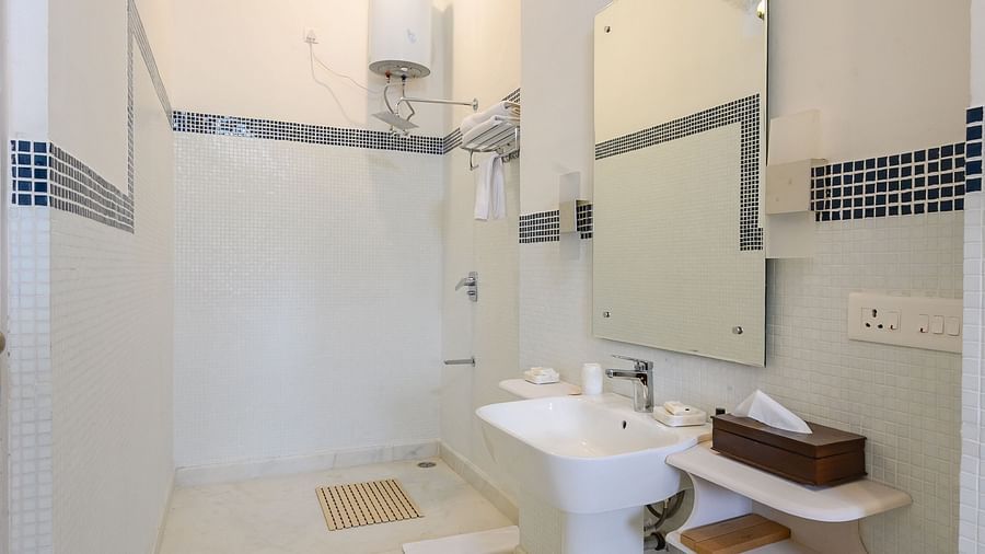 A narrow bathroom featuring a white sink, a mirror, a shower, and a blue accent on the ceiling, taken in a vertical shot - Tijara Fort-Palace - 19th Century, Alwar.