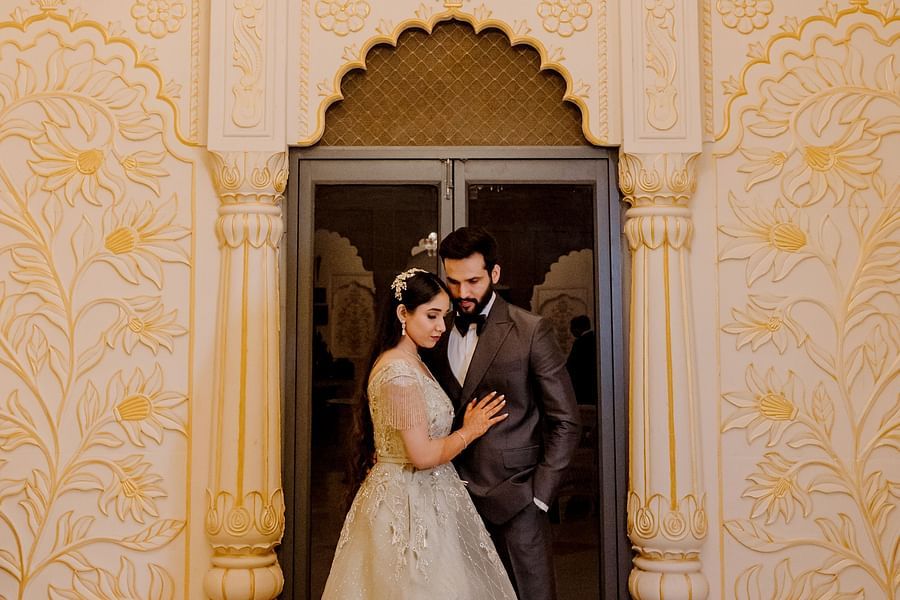 A couple stands together below a chandelier in an elegant room at  Umaid Palace - Best Luxury Heritage Resort Near Jaipur.