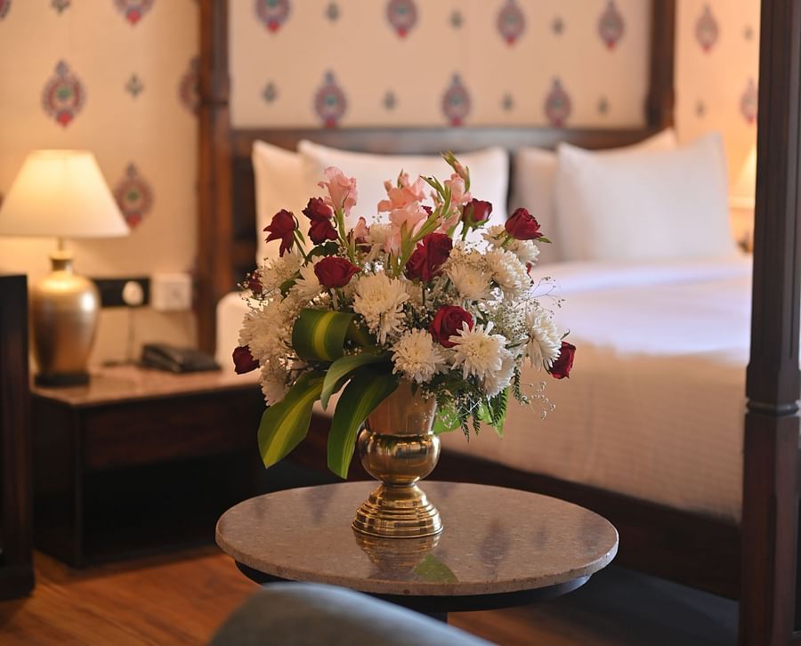 A  Premium Tent featuring a flower vase placed on a table and at the background there is a bed, a bedside table with lamp and a telephone at The Baagh Ananta Elite, Ranthambore