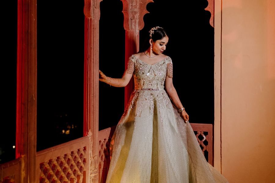 The bride stands in a balcony, wearing an elegant gown, illuminated by soft lighting- Umaid Palace - Best Luxury Heritage Resort Near Jaipur. 