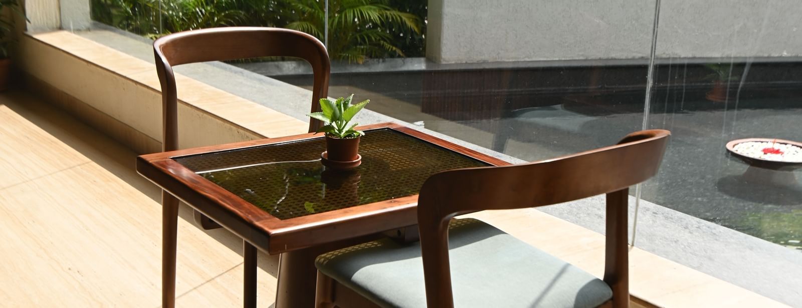 A small wooden table and chairs are positioned near a window with a view of an outdoor area | Vedic Village Spa Resort, Kolkata