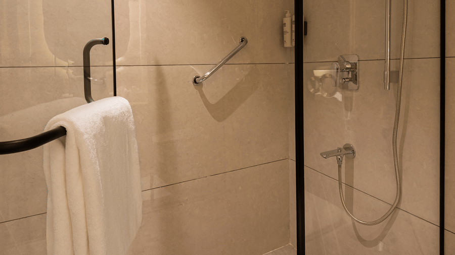 A modern bathroom area featuring a glass walk-in shower cubicle with chrome fittings and white towels at Ananta Express, Katra.