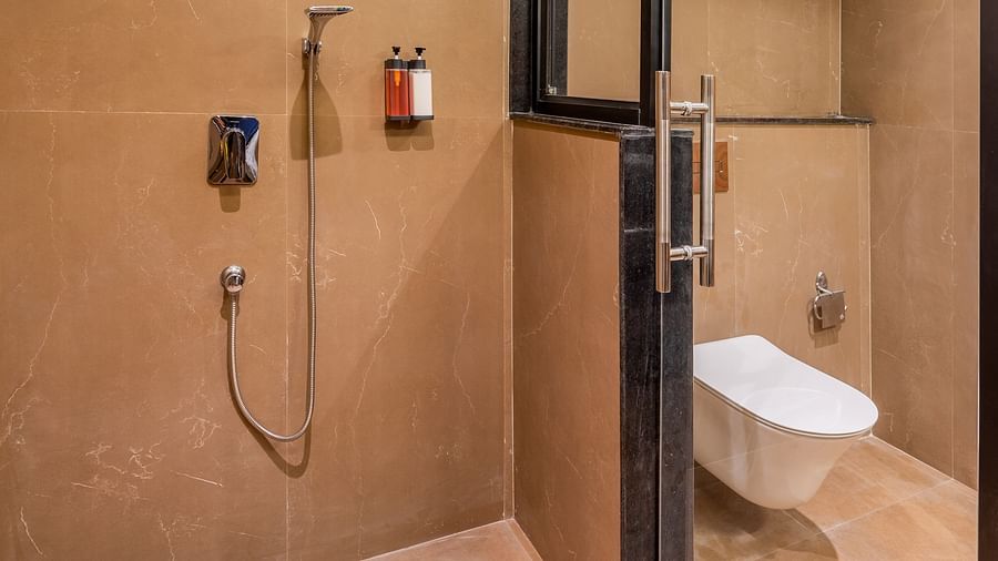 Bathroom at vishranti Hotel, Dehradun featuring shower area, a toilet,  a mirror with ambient lighting.