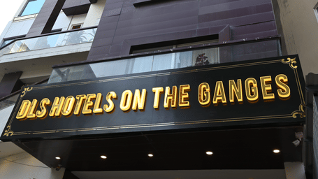 Exterior view of DLS Hotels on the Ganges, showcasing the multi-story purple building, the hotel signage in bold yellow letters, and the surrounding urban environment, giving a clear impression of the hotel’s façade