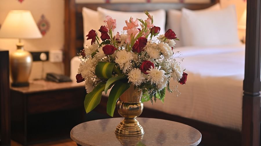 A  Premium Tent featuring a flower vase placed on a table and at the background there is a bed, a bedside table with lamp and a telephone at The Baagh Ananta Elite, Ranthambore