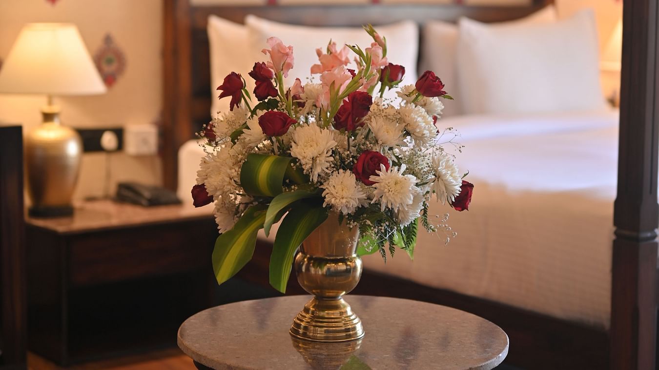 A  Premium Tent featuring a flower vase placed on a table and at the background there is a bed, a bedside table with lamp and a telephone at The Baagh Ananta Elite, Ranthambore