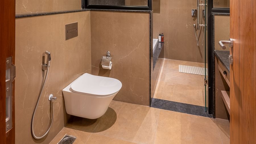 Side shot of a bathroom at vishranti Hotel, Dehradun featuring shower area, a toilet,  a mirror with ambient lighting.