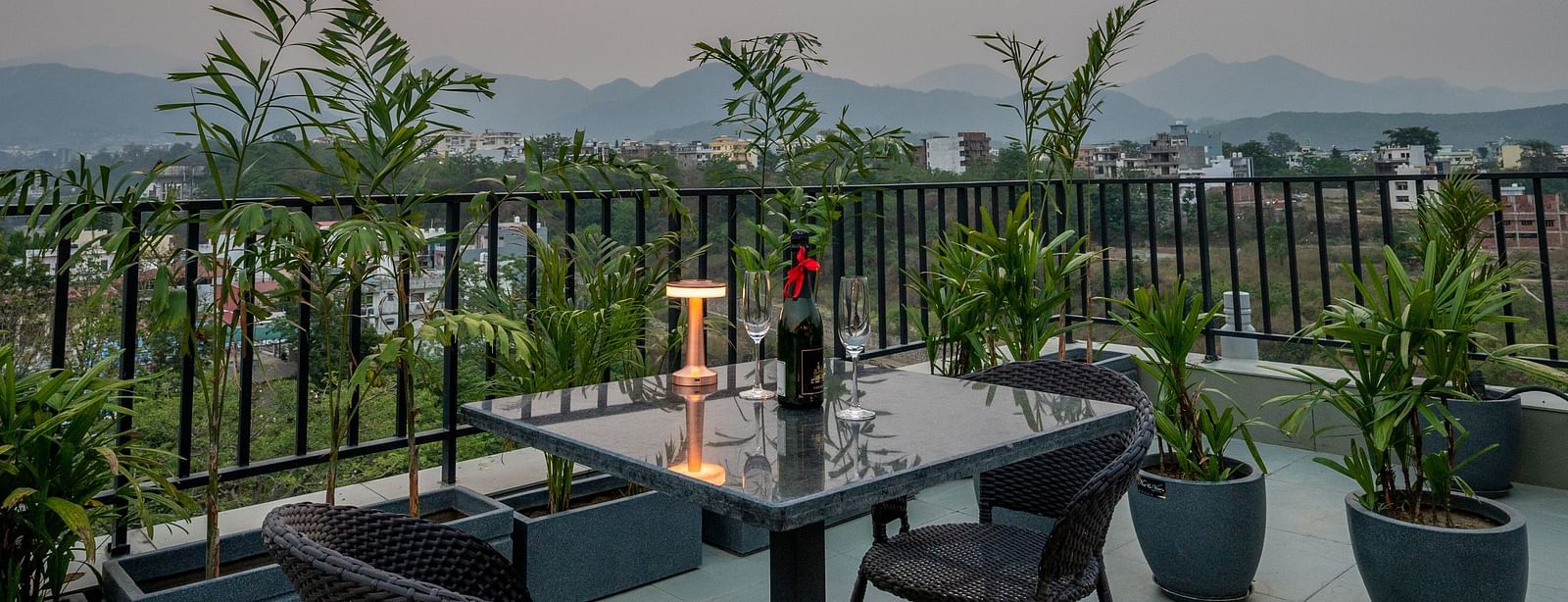 Close up of an outdoor seating area at Vishranti Hotel, Dehradun with a seating area features multiple tables with chairs, and plants are visible in the background.