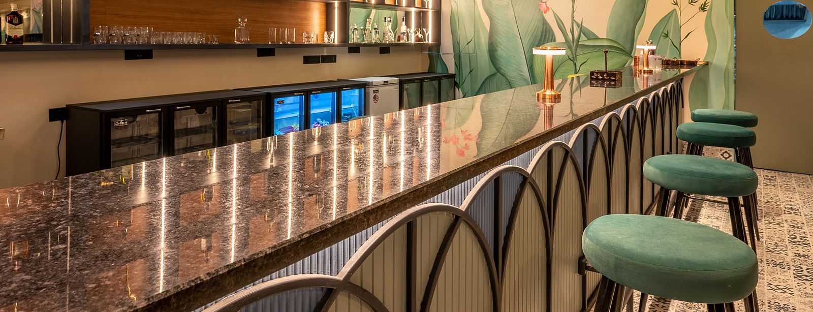 A bar featuring a long bar counter with stools, a well-stocked back bar, and decorative ceiling panels at Vishranti Hotel, Dehradun.