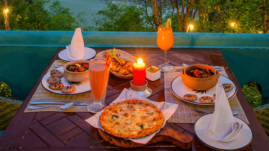 A candlelit outdoor dining table laden with food overlooking the river at Neemrana's Glasshouse on The Ganges - 21st Century, Rishikesh.