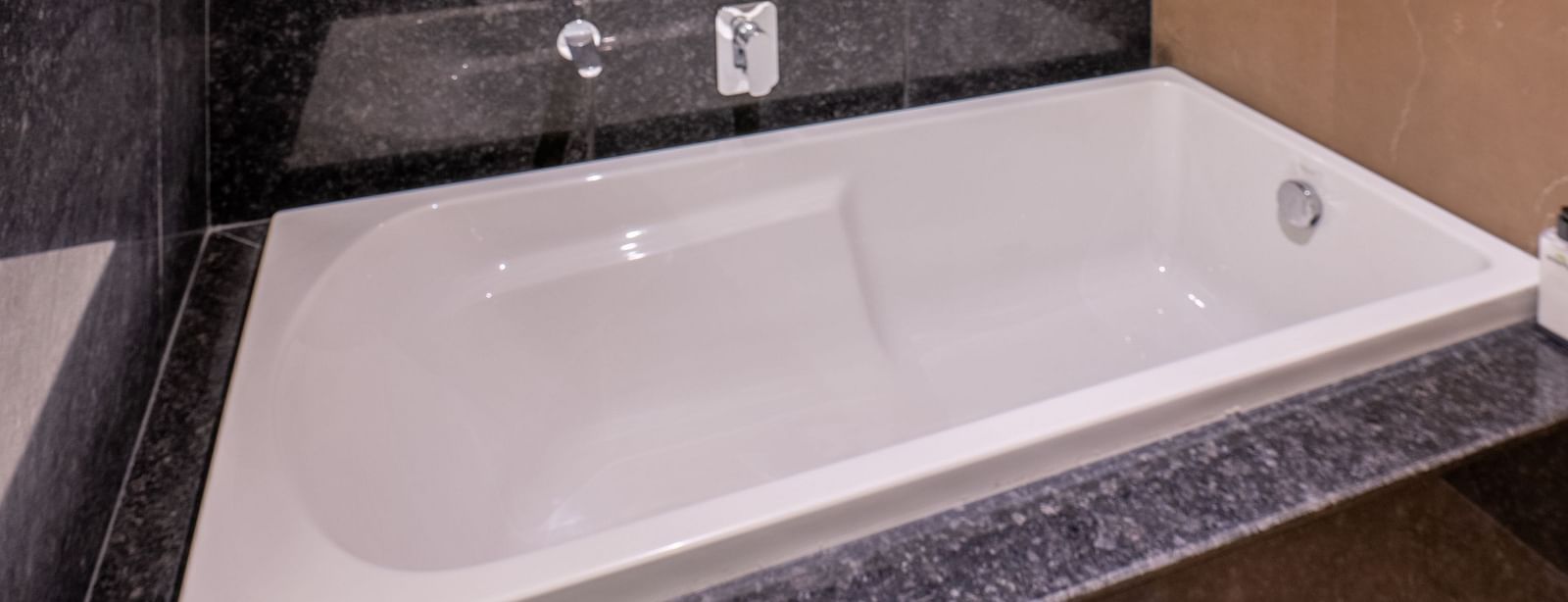 Shot of a white bathtub in Suite of Vishranti Hotel Dehradun with black marble walls.