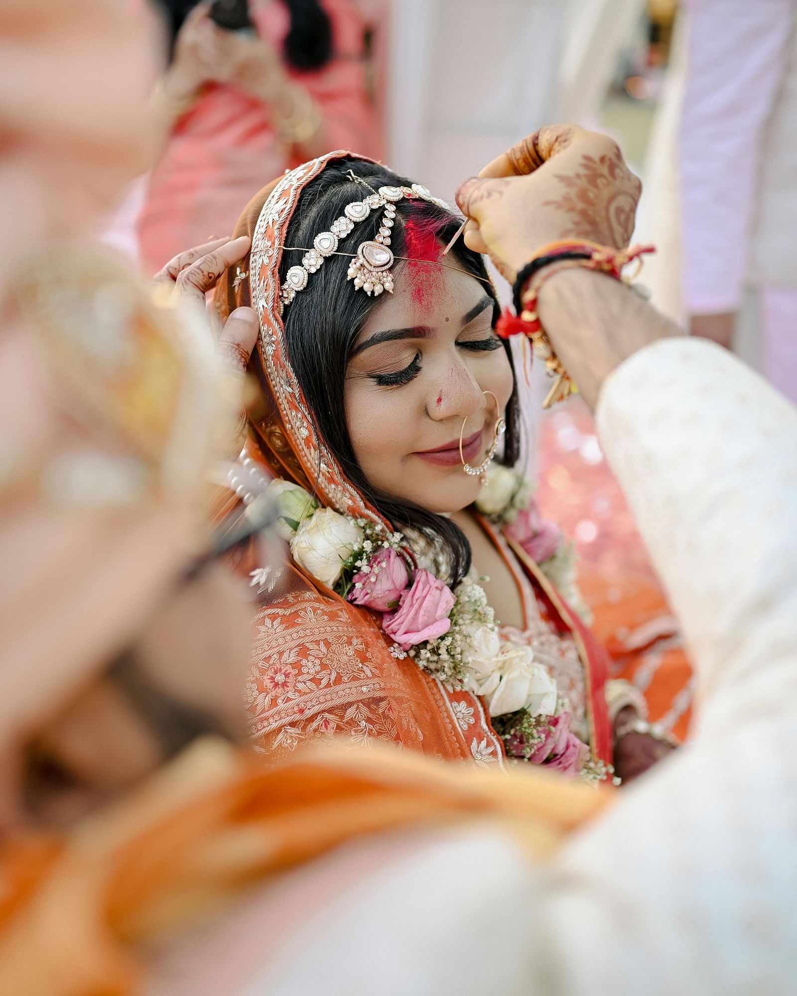 A close-up of a woman in traditional wedding attire, with a veil and jewelery, during a ceremonial moment at a wedding