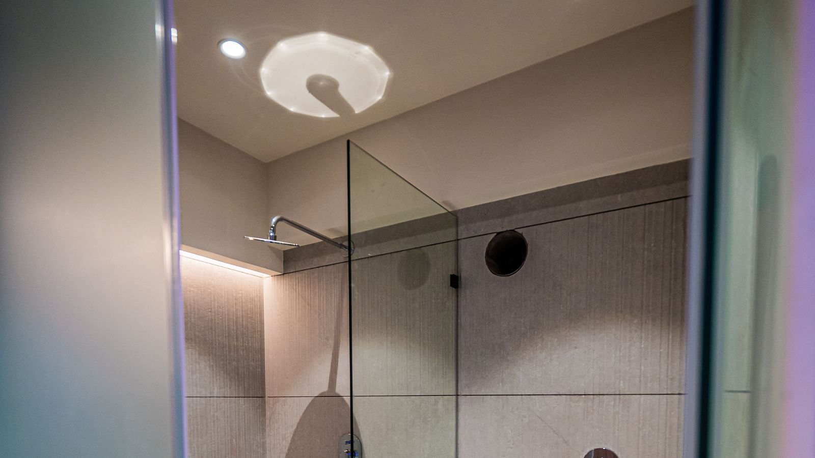 A western toilet separate from the shower area, enclosed with glass panels, at Indie Stays Mumbai International Airport.