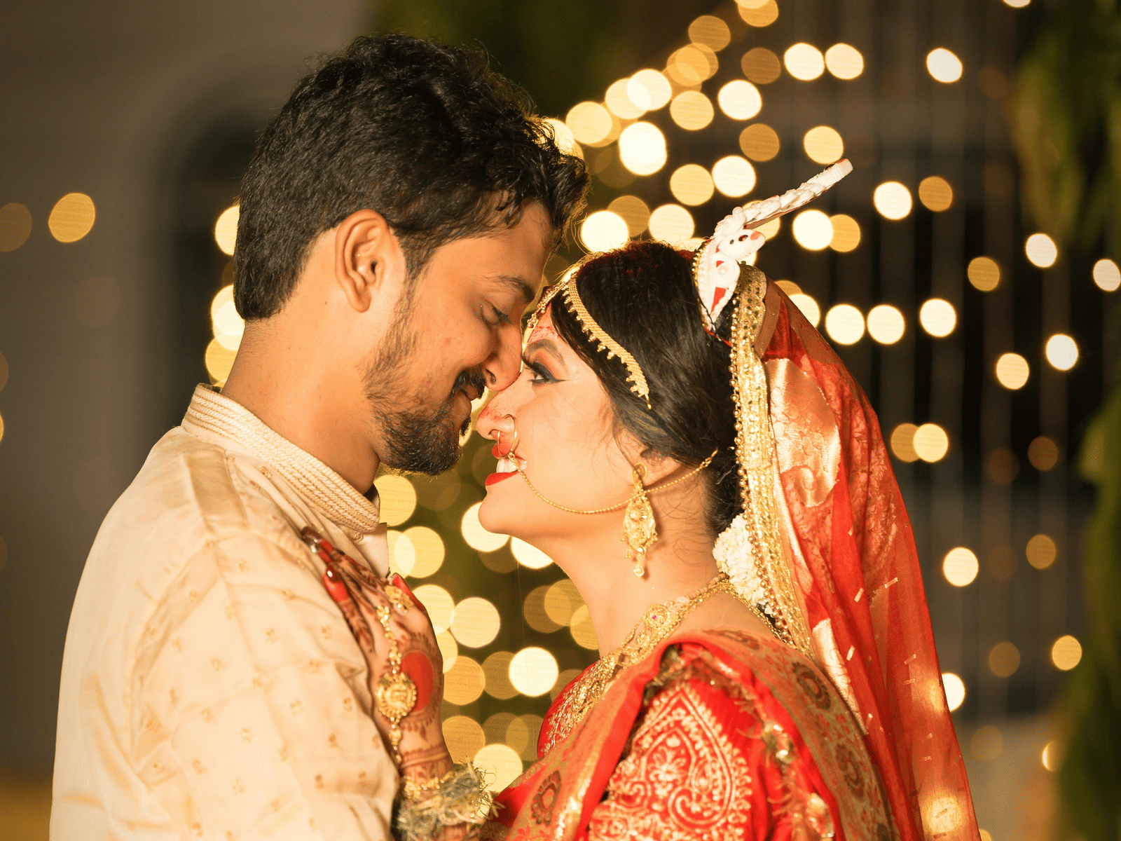 A bride and groom sharing a romantic moment adorned with garlands and lights during their wedding ceremony.