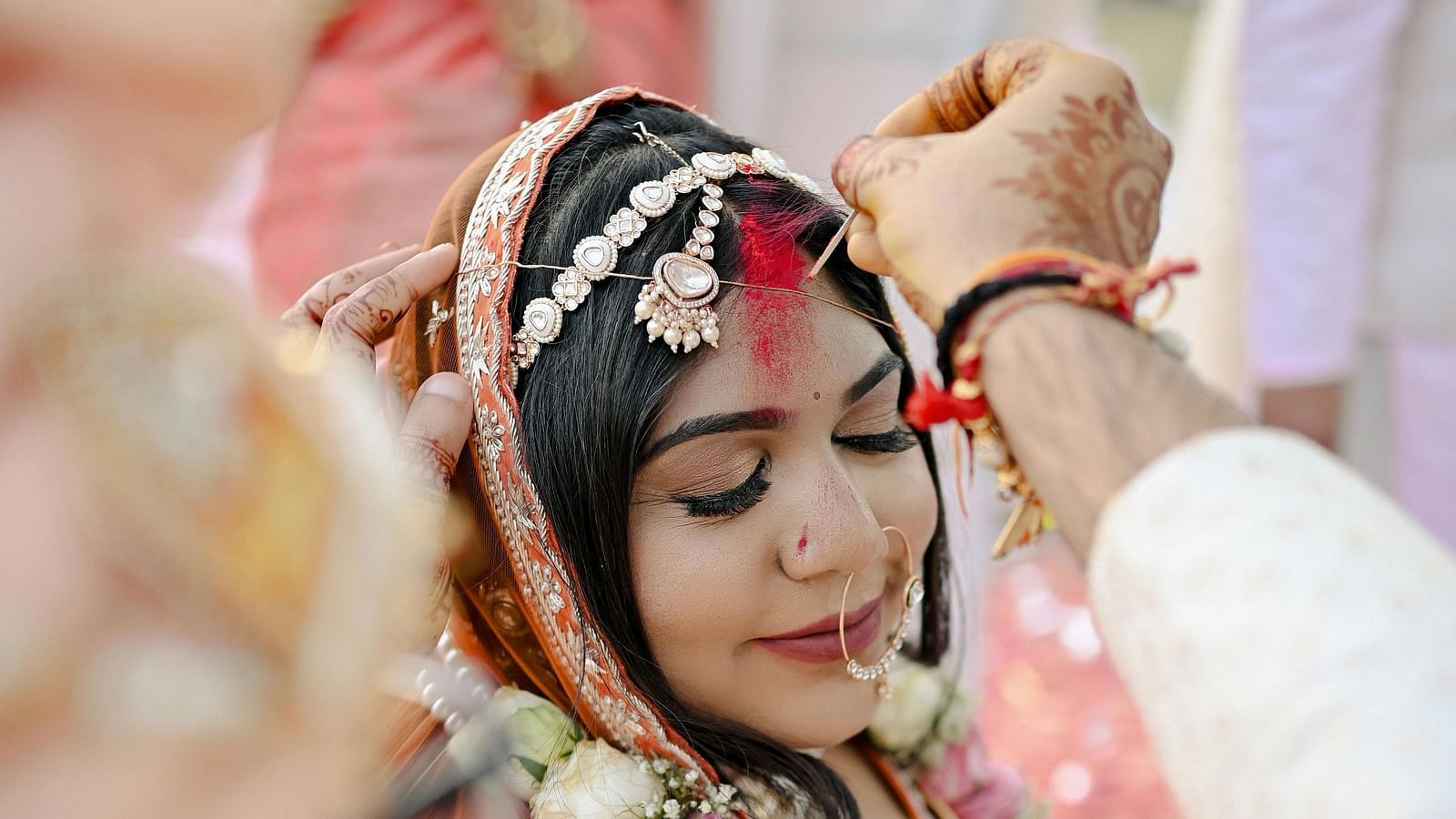 A close-up of a woman in traditional wedding attire, with a veil and jewelery, during a ceremonial moment at a wedding
