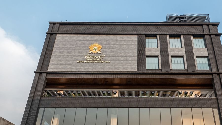 Low angle shot of the facade of Vishranti Hotel Dehradun showcasing its logo engraved on the wall taken during the day.
