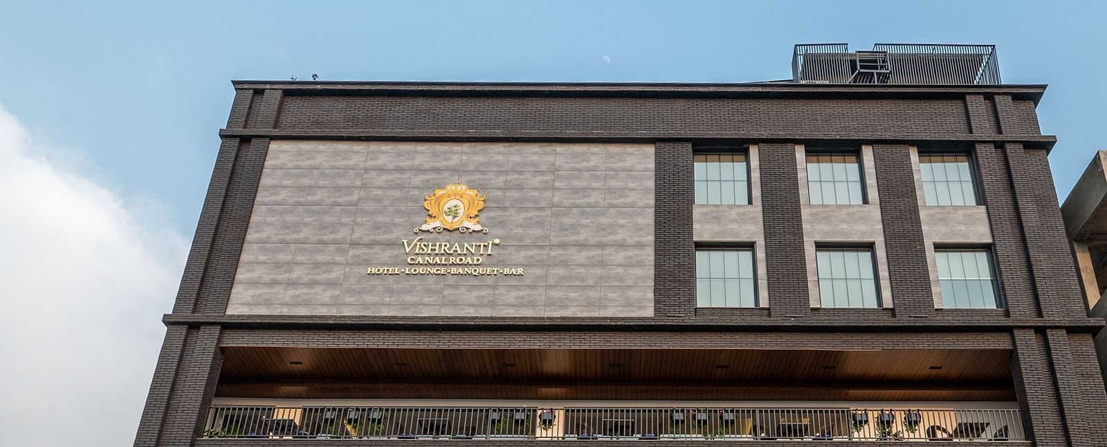 Low angle shot of the facade of Vishranti Hotel Dehradun showcasing its logo engraved on the wall taken during the day.