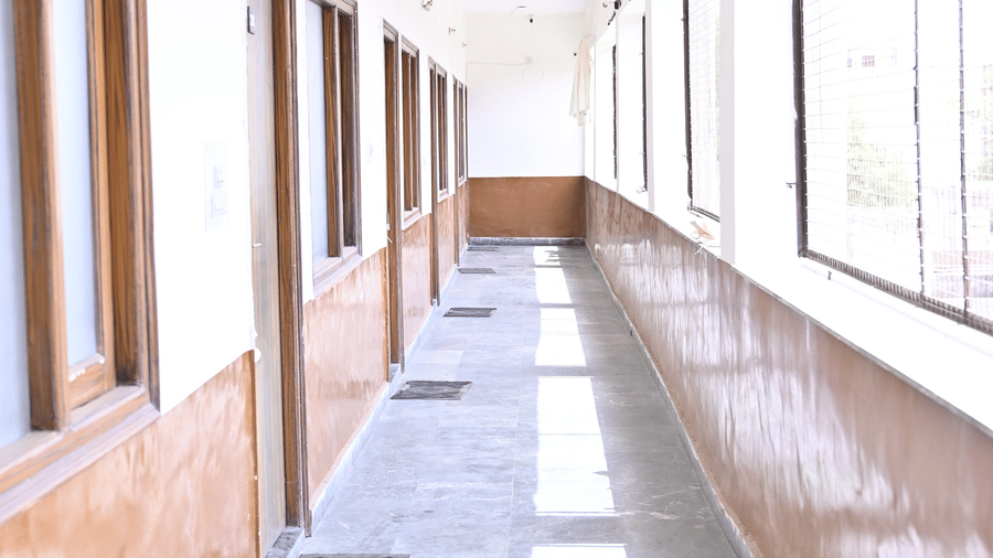   A long hallway in a  hotel with open glass windows at one side and doors to rooms at one side - Hotel Goverdhan, Agra