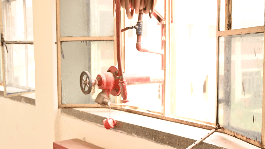 A hallway with large windows, with a fire hose reel and a cabinet below containing fire extinguishers - Hotel Goverdhan, Agra