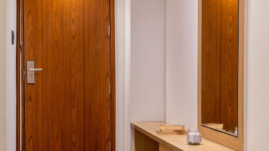 Entrance of a room at Vishranti Hotel, Dehradun featuring a wodden door, a mirror and a side table.